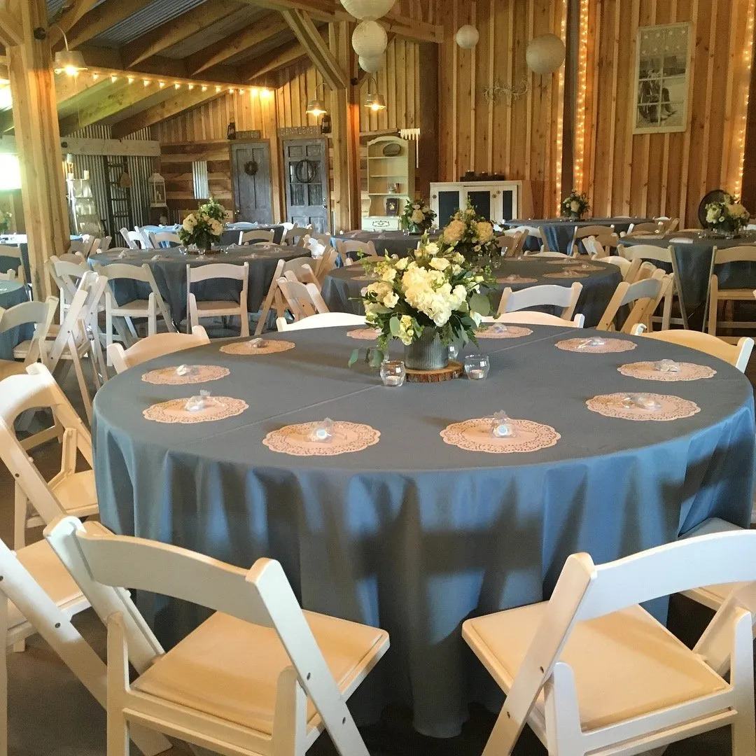 Round reception tables with blue linens, white chairs and floral centerpieces inside the barn