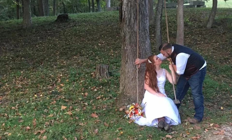 Groom leaning in to kiss the bride as she sits on a rope swing in the woods